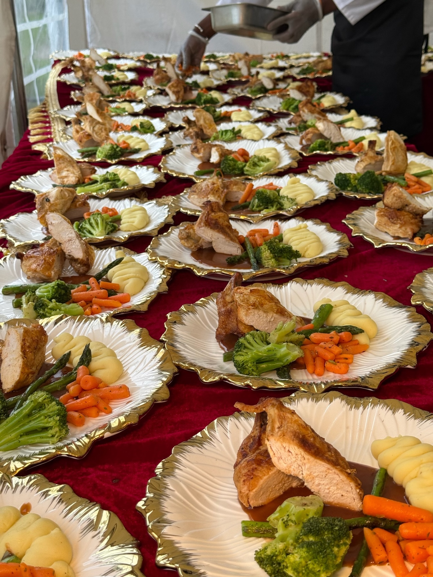 Plated chicken banquet on gold-rimmed plates across a burgundy marquee table