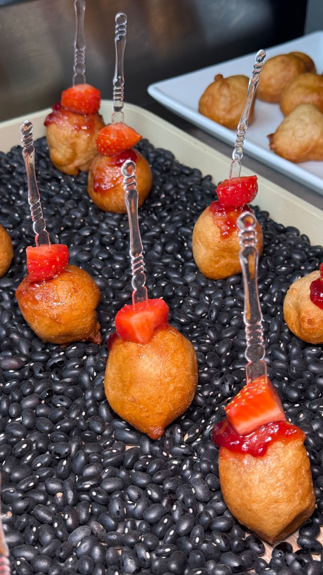 Golden puff puff topped with strawberry on a black bean display